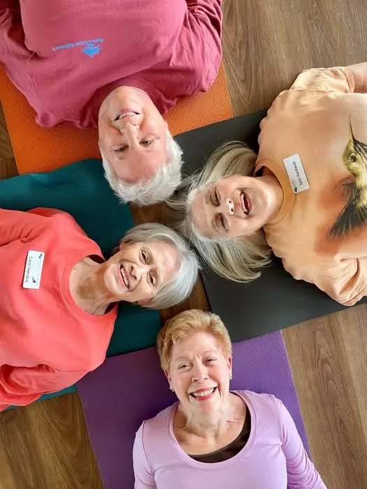 Four Trinity Terrace female residents in the fitness center laying down with their heads together smiling